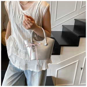 Détail d'un sac à main argenté métallisé avec nœud rose et breloque perle cœur