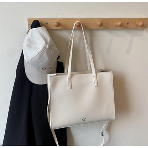 Detail of minimalist cream tote bag showing pebbled leather texture and adjustable strap
