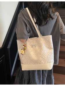 Large beige tote bag with geometric texture and silver bow shown on a shoulder