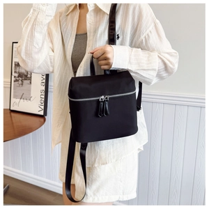 Close-up of black nylon backpack featuring dual silver zippers and leather top handle detail