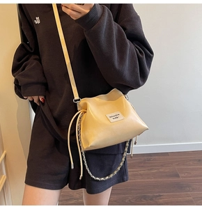 Detail of light beige drawstring crossbody bag with silver chain and white woven label