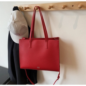 Detailed view of large red tote bag in lychee pattern leather hanging on wood rack