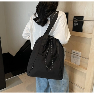 Detailed view of black nylon drawstring tote bag with letter label shown on a model