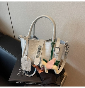 Detail of light gray crocodile texture handbag with silver lock and pegasus charm