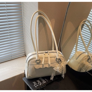 Detail view of cream shoulder bag with wavy edge trim and elegant pearl bow charm