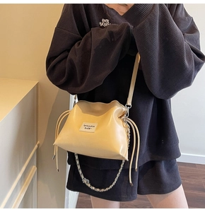 Detail of cream drawstring bucket bag with leather texture and metal chain strap