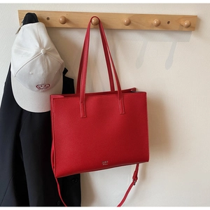 Close-up of red pebbled leather tote bag hanging on wooden hook with metal brand detail