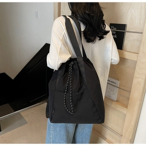 Detail of black drawstring backpack showing nylon texture and side pocket on a model