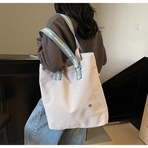 Close-up of a grey canvas tote bag featuring a contrast blue and yellow lettered strap