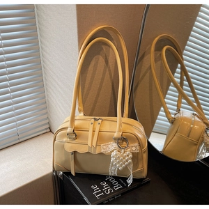 Detail view of cream Boston bag with double straps, wavy flap, and pearl bow charm