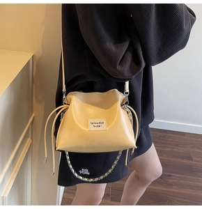 Model showing beige soft leather drawstring bucket bag with silver metal chain strap