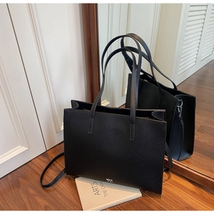 Detail of a black pebbled leather tote bag with MER PAI logo on a wood floor