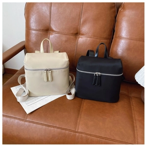 Mini nylon backpacks in black and beige displayed on a brown leather sofa