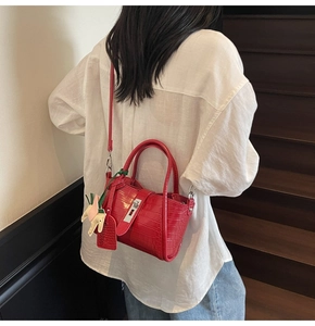 Detail of red crocodile pattern handbag with metal clasp worn by a model on stairs