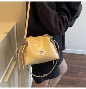 Detail of cream yellow glossy leather bucket bag with chain strap and brand label
