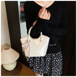 Détail du sac seau en cuir verni crème avec logo, ruban rose et breloque en perle