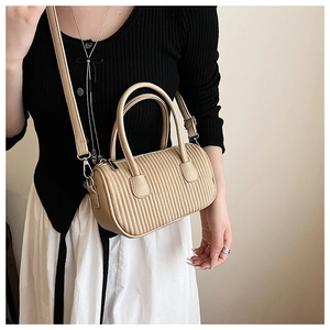 Close-up of beige pleated cylinder bag with detailed texture on white dress background