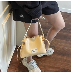 Detail of yellow bucket bag with drawstring closure and metal chain shoulder strap