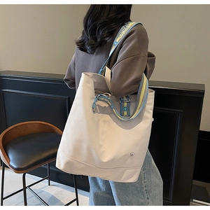 Detail of a large beige canvas tote bag featuring a stylish patterned wide shoulder strap