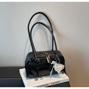 Detail of black leather shoulder bag with twin zippers and a pearl heart charm on a book