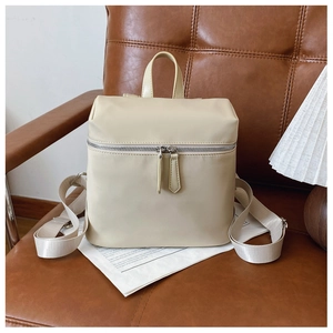 Detail view of cream nylon backpack with dual zippers on a leather seat