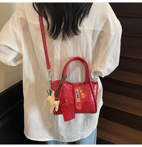 Detail of red crocodile pattern bucket bag with metal lock and horse charm on model