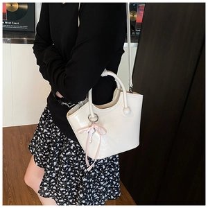 Détail du sac seau en cuir blanc avec nœud en soie rose et logo embossé