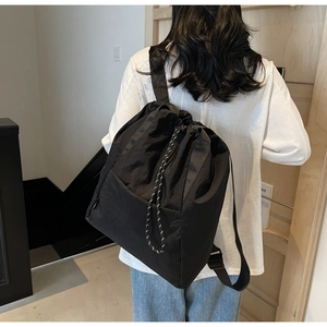 Detailed view of black nylon drawstring backpack with plaid texture on female model
