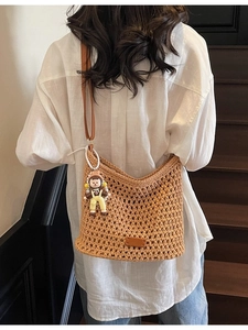 Handmade khaki woven shoulder bag with cartoon doll charm shown on model in indoor setting