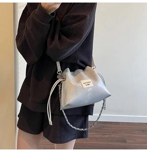 Macro detail of silver bucket bag with logo tag, drawstring closure and chain strap