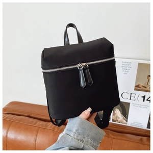 Detail view of the sleek dual silver zippers and top handle of a black nylon backpack