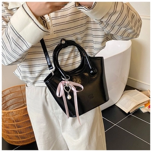 Detail of black glossy bucket bag featuring pink ribbon bow and pearl heart charm pendant