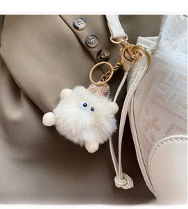 Detail of white plush monster keychain with brown knit hat on a texture handbag