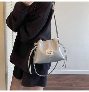 Detail of silver metallic bucket bag with drawstring closure and chain strap on model