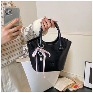 Détail du sac seau noir en cuir verni brillant avec breloques cœur, perle et ruban rose