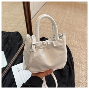 Detailed view of white bucket bag with pleated closure and dual cylindrical handles