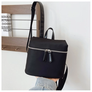 Detail of a minimalist black nylon backpack with dual silver zippers and top handle