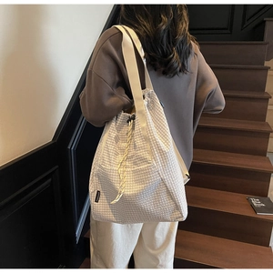 Detail of grid texture tote bag with drawstring closure and brand label on strap