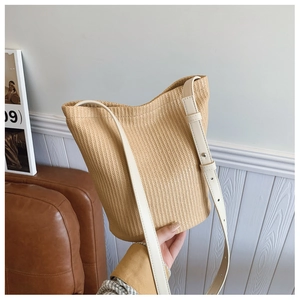 Detail of hand-woven straw bucket bag with adjustable cream leather strap and metal studs