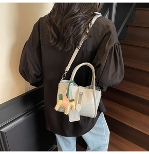 Detail of light gray crocodile pattern handbag with horse charm on indoor stairs