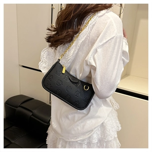 Detail of black leather shoulder bag with embossed monster pattern and gold chain strap