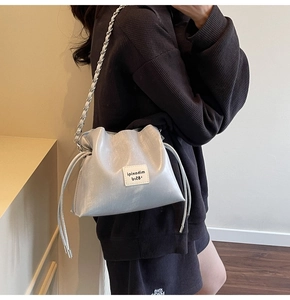 Detail of silver metallic drawstring bucket bag with woven chain strap and fabric patch