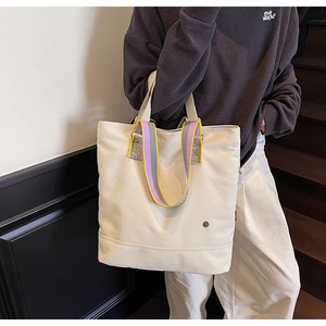 Detail of off-white canvas tote with purple-yellow straps and metal badge ornament