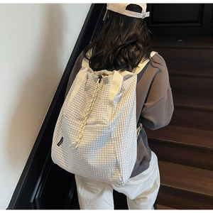 Close-up of white plaid drawstring backpack with woven straps and textured fabric detail