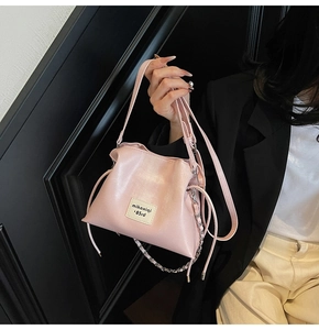 Close-up of pink bucket bag with drawstring closure, silver chain, and logo patch detail