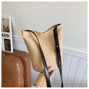 Detail of hand-held straw bucket bag with dark brown leather strap and woven texture