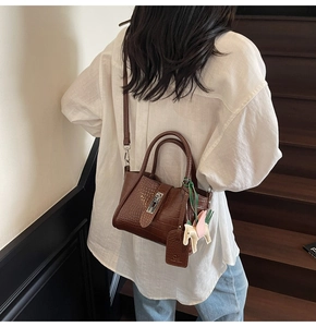 Detail of dark brown crocodile pattern handbag with metal lock and horse charm on a model