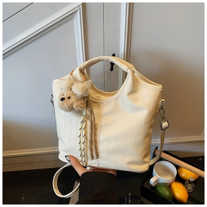 Detail of cream crocodile embossed handbag with metal hardware and plush animal charm
