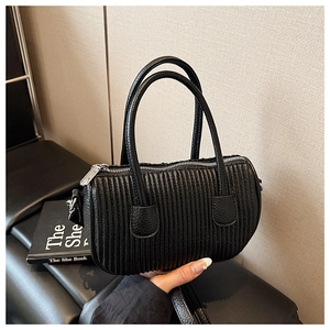 Detail of black pleated cylindrical bag with top handles and sleek metallic zipper