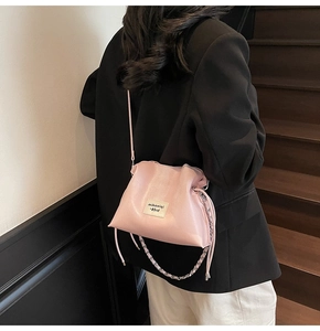Detail of light pink bucket bag featuring a white cloth label and metal chain strap